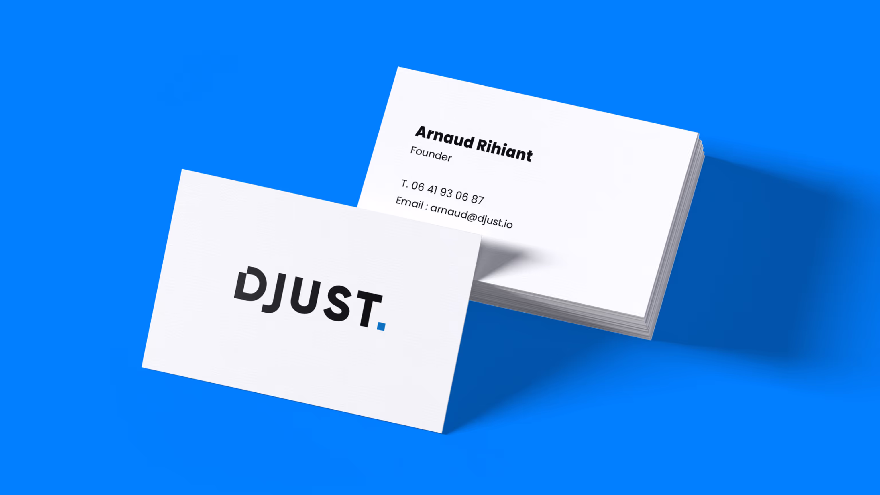 Maquette de cartes de visite blanches DJUST sur fond bleu, montrant le logo au recto et les coordonnées d'Arnaud Rihiant au verso